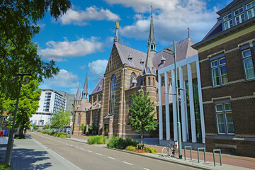 Eindhoven, Netherlands - July 17. 2022: City street with medieval gothic augustine church and marienhage hotel, blue summer sky fluffy clouds