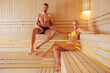 © dusanpetkovic1 - Romance, wellness, and spa concept. A happy romantic couple in swimwear sitting on the bench in a hot sauna in the spa center, holding hands and relaxing.