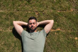 © Manuel - Young and handsome man, with a beard and green shirt, with his eyes closed and his hands behind the back of his neck lying on the grass, resting. Concept beauty, fashion, trend, sleep.