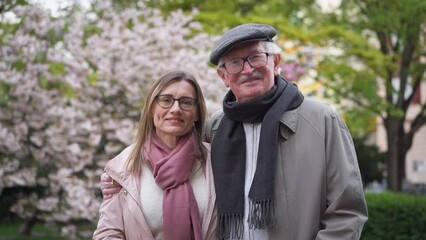 Wall Mural - Adult daughter hugging her senior father outdoors in park on spring day.