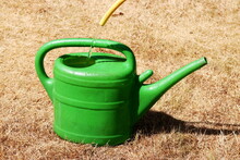 Drought Effected Grass With Green Watering Can Being Filled With A Hose.