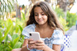 © Danko - Beautiful little brunette girl in summer day outdoor using smart phone.