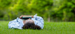 © Akarawut - African American woman is lying down in the grass lawn inside the public park holding book in her hand during summer for reading and education concept with copy space