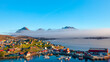 A layer of fog spreads between the mountains and the sea -Picturesque village and Colorful houses on coast of Greenland - Tasiilaq, East Greenland