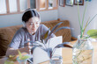 明るい植物のある窓辺の部屋でノートパソコンでオンライン授業,リモートワークをする日本人女性