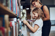 © Przemek Klos - Teacher helping to choose book her schoolgirl in school library. Smart girl selecting literature for reading. Books on shelves in bookstore. School education. Benefits of everyday reading
