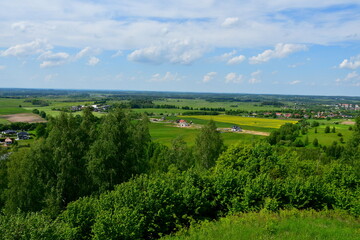 Wall Mural - A view from the top of a tall hill or mountain with vast fields, meadows, forests, moors, and other types of flora visible, with a lake, some urban settlements, and other buildings in the distance