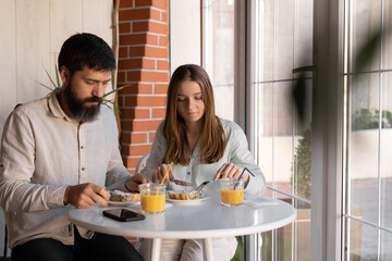 Wall Mural - cheerful young couple out for breakfast in a cafe before work, sitting near window and enjoying conversation. woman and her boyfriend talking and laughing during meal