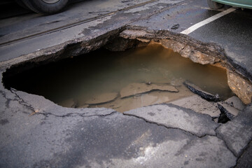 Wall Mural - Huge sinkhole on busy asphalt road surface on which cars drive. Accident situation on a city street due to cracks in asphalt. Broken hole filled with muddy water.