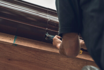 A handy man uses a pop rivet gun to fasten two pieces of a steel gutter together. Roof construction or renovation.