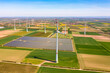 Panorama von Solarmodulen eines Solarparks als Freiflächenanlage inmitten von Windrädern zwischen landwirtschaftlichen Feldern in Deutschland