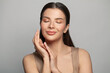 © millaf - Attractive young spa model woman holding her hands near her face and smiling against grey wall background, skincare concept