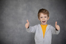 Portrait Of Beautiful Little Boy Giving You Thumbs Up Over Modern Gray Background