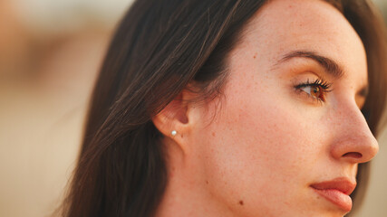 Beautiful brown-haired woman with long hair is stands on the beach. Gorgeous girl with freckles and long eyelashes.