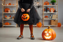 Kid Going Trick Or Treating. Low Section Shot Of Child In Festive Halloween Costume Next To Cute Jack-o-lantern. Girl In Black Tulle Skirt And Striped Witch Stockings Holding Orange Pumpkin Basket