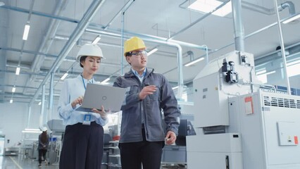 Poster - Portrait of Two Young Asian Heavy Industry Engineers in Hard Hats Standing with Laptop Computer and Discussing Work Process in a Factory. Two Manufacturing Employees Chatting in Production Facility.