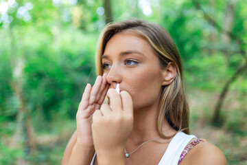 Woman using nasal spray outdoors for tree pollen allergy treatment