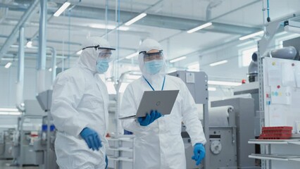 Poster - Two Scientists Standing in a Heavy Industry Factory in Sterile Coveralls and Face Masks, Using Laptop Computer. Examining Industrial Machine Settings and Configuring Production Functionality.