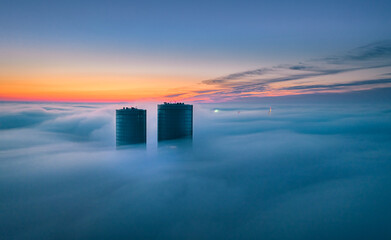 Skyscraper rooftop over the clouds at sunrise. Thick fog covers the Riga city, and warm sunlight over the clouds and church tower.