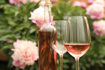 Sticker - Glasses and bottle with rose wine against beautiful peonies, closeup. Space for text