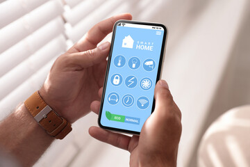 Man using Smart Home app on mobile phone indoors, closeup