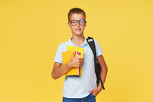 Portrait Of A Schoolboy In Glasses With Textbooks And A Backpack On A Yellow Background. Back To School