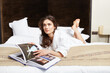© Dragosh - Cheerful brunette young woman relaxing on a bed. Young beautiful woman wearing white bathrobe in bedroom.