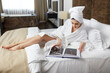 © Dragosh - Beautiful caucasian woman in soft bathrobes with towel on hier head, browse a magazines, lying dowmn on bed.