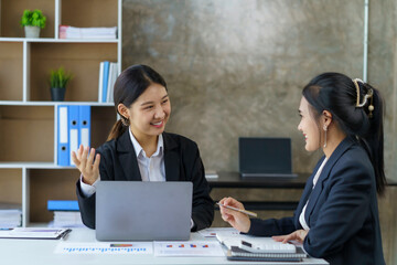 Wall Mural - Two young Asian businesswomen discuss with new startup project Idea presentation, analyze planning and financial statistics and investment market on laptop computer at office.