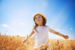 Happy girl walking in golden wheat, enjoying the life in the field. Nature beauty, blue sky and field of wheat. Family outdoor lifestyle. Freedom concept. Cute little girl in summer field