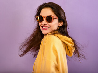 Relaxing smiling woman posing in fashion yellow hoodie in summer fashion sun glasses in hood on the head on purple bright background with empty copy space. Happy closeup