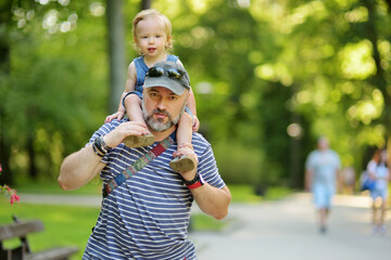 Wall Mural - Cute toddler boy in his fathers arms. Dad and son having fun on sunny summer day in the city.