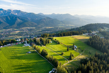 Aerial view of Zakopane town underneath Tatra Mountains taken from the Gubalowka mountain range. High mountains and green hills in summer or spring.