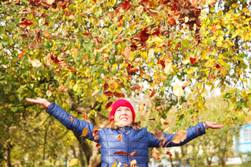 Defocus autumn people. Teen girl raising hand and throwing leaves. Many flying orange, yellow, green dry leaves. Joy autumn. Happy fall. Out of focus