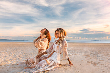 Wall Mural - two beautiful young woman in elegant boho dresses outdoors at sunset