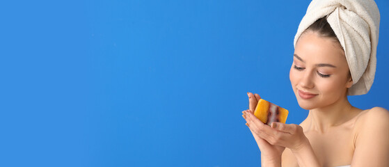 Canvas Print - Beautiful young woman holding soap bar on blue background with space for text