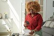 © AnnaStills - African serious girl with curly hair scanning qr code on receipt for payment online using her mobile phone