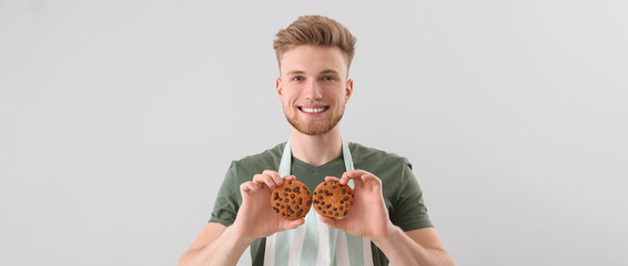 Wall Mural - Handsome male baker with fresh cookies on light background