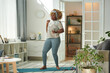 © AnnaStills - African girl standing on exercise mat and dancing to music during sports training at home
