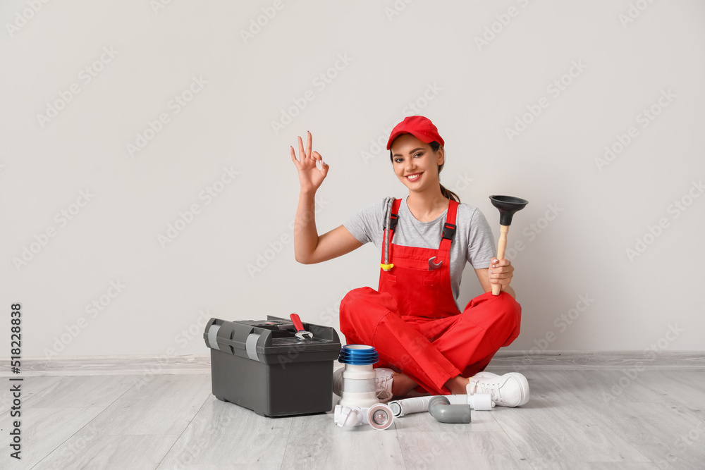 Female plumber with tools and bag showing OK near light wall