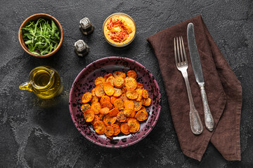 Composition with bowl of tasty baked carrots and ingredients on dark background