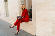© Svetlana Sokolova - Beautiful smiling woman  in  elegant red velvet suit holding purse and  posin outdoor in old european city.    Blond wavy hairs, perfet skin, full lips.
