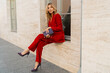 © Svetlana Sokolova - Beautiful smiling woman  in  elegant red velvet suit holding purse and  posin outdoor in old european city.    Blond wavy hairs, perfet skin, full lips.