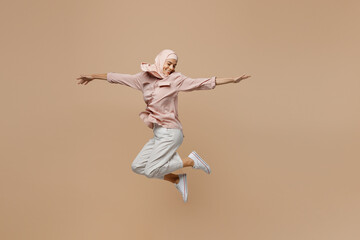 Wall Mural - Full body young fun arabian asian muslim woman she wear abaya hijab pink clothes jump high with outstretched hands isolated on plain pastel light beige background. People uae islam religious concept.