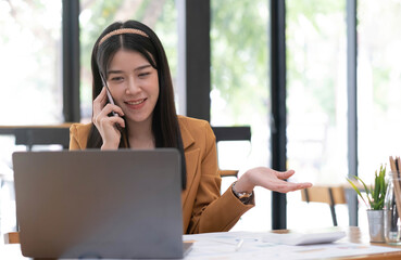 Asian business woman have the joy of talking on the phone, laptop and tablet on the office desk.