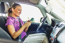 Nurse Arriving At A Patient's Home, She Is Sitting In Her Car Using Her Mobile Phone. A Nurse Dressed In Her Scrubs Uniform Sitting In Her Stationary Car, Holding Her Mobile Phone.