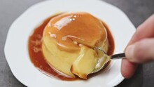 A female hand with a spoon breaks a piece of classic creme caramel.
