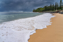 Low Angled View Of White Foamy Waves On A Sandy Beach With Dark Storm Clouds On The Horizon