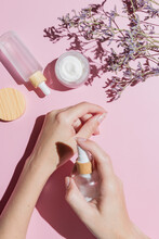 Woman Applying Cream On Cer Hand Ower Pink Background With Cosmetic Products And Flowers. Skin Care Treatment Concept