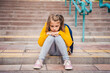 © velirina - Back to elementary, primary school. Little sad unhappy girl with backpack. Lonely schoolgirl with emotional problems, victim of bullying in schoolyard. Teen in depresiion sitting alone on stair steps